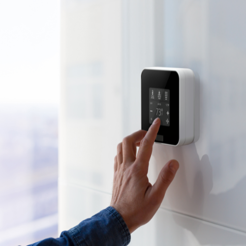 Guests hand touching the screen of the EOS Smart Thermostat to adjust hotel room temperature and climate settings.
